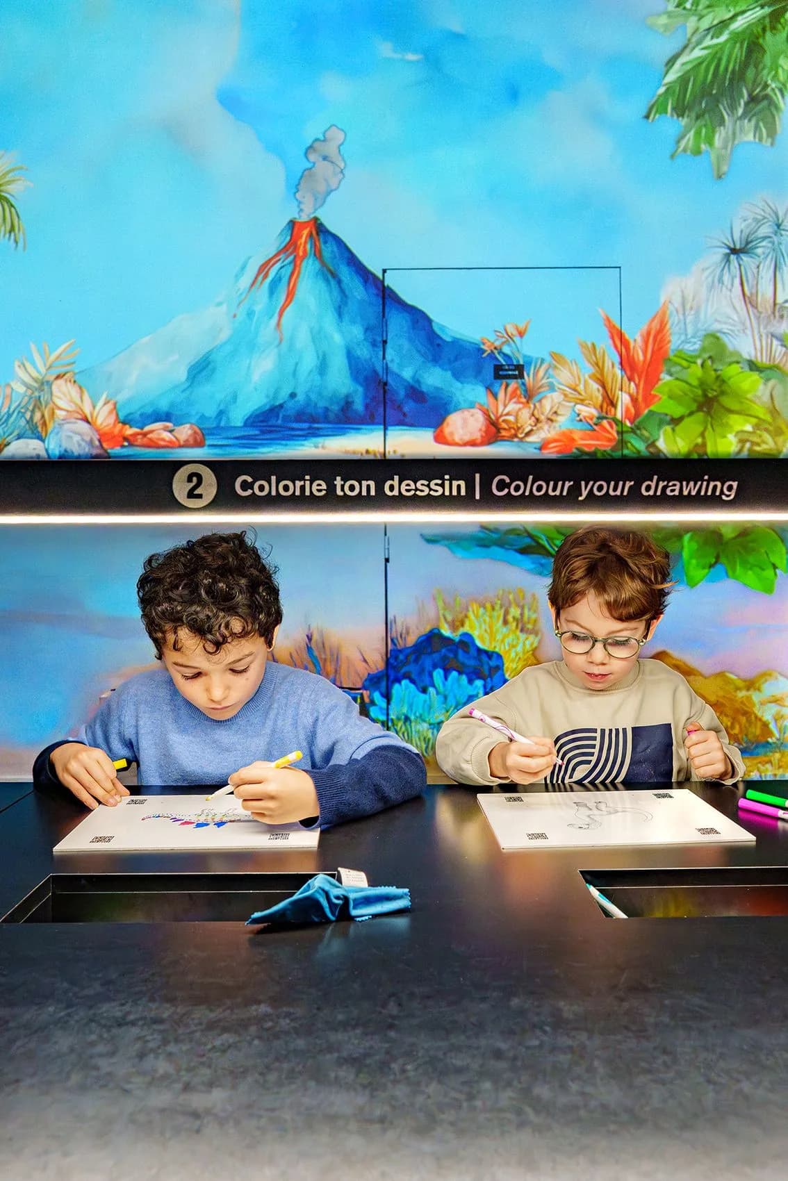 Deux enfants colorient leurs dessins devant la projection immersive